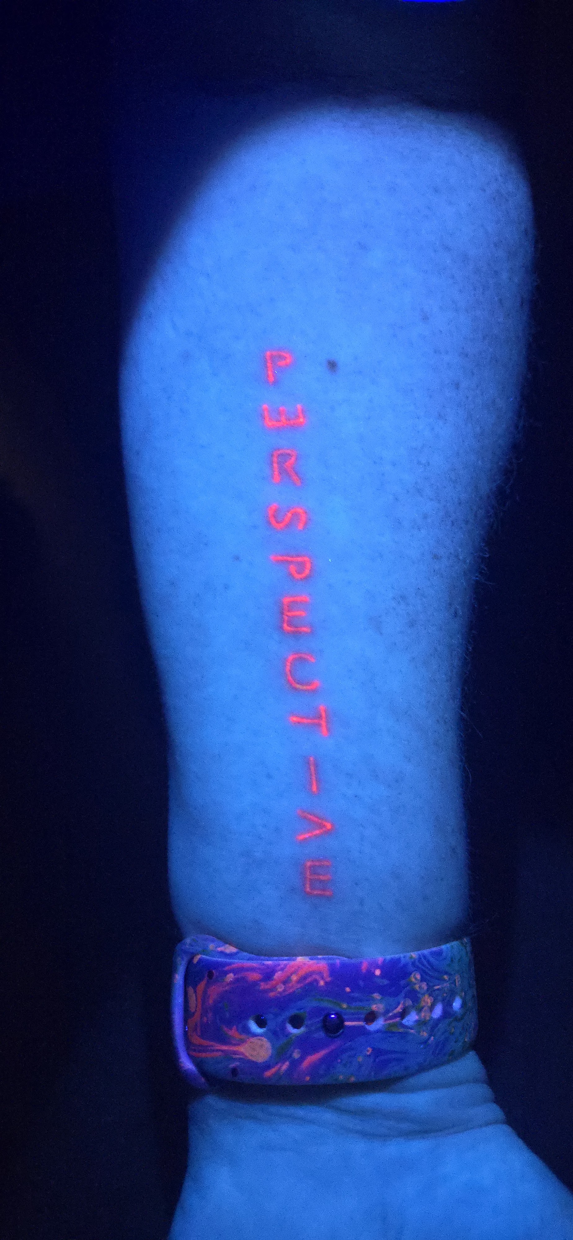Blacklight lettering tattoo glowing under UV light